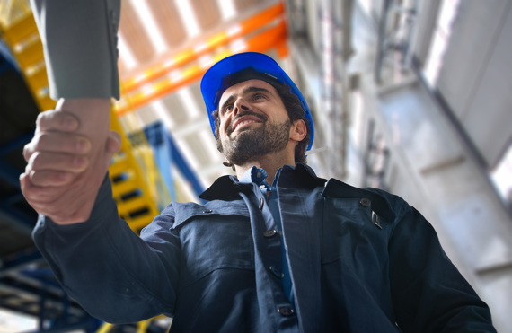 Construction worker in blue hard hat smiling and shaking hands indoors.