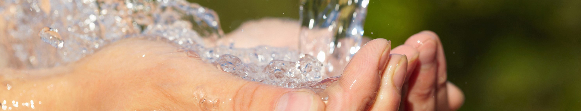 Hands cupped under flowing water against a blurred natural background.