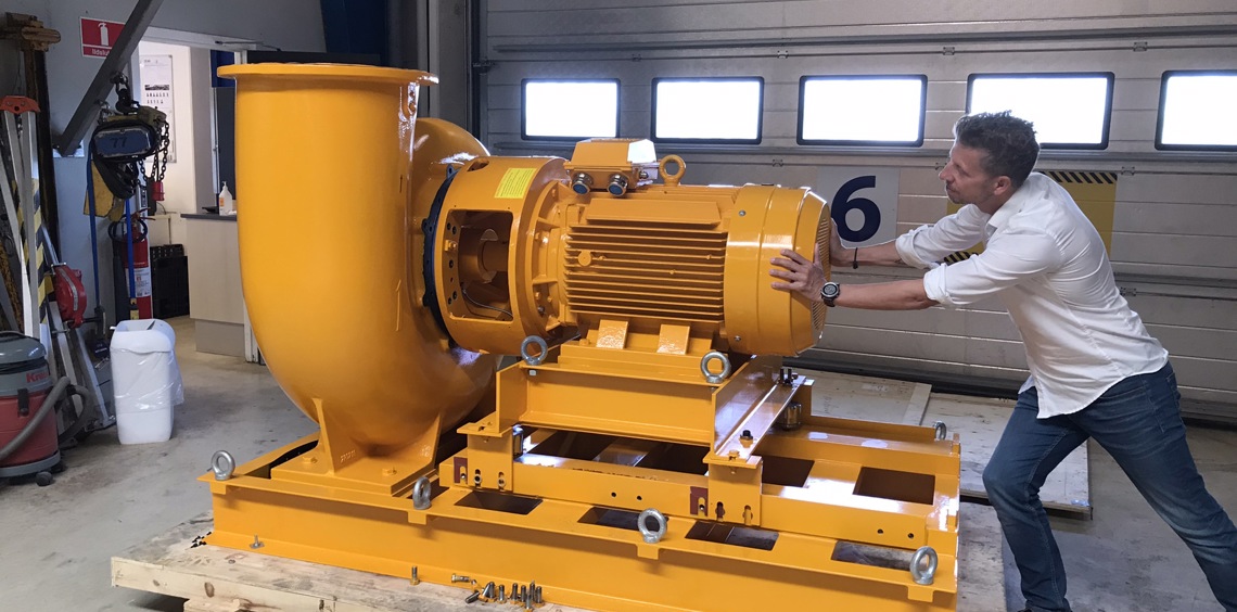 Man pushing large yellow industrial pump inside a workshop.