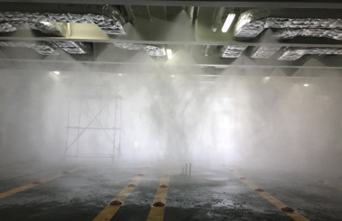 Sprinkler system testing in an industrial setting with mist and scaffolding.