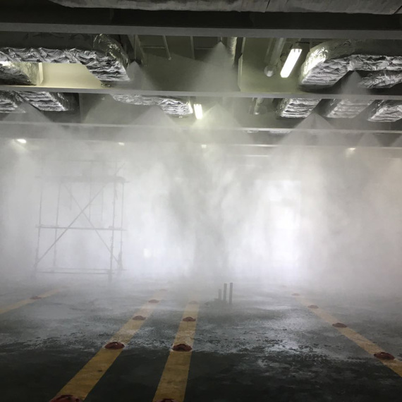 Sprinkler system testing in an industrial setting with mist and scaffolding.