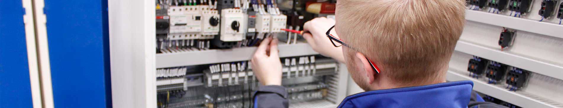 Technician working on electrical control panel with various switches and wires.