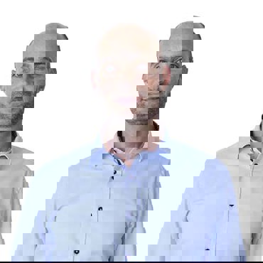 Man in a light blue shirt smiling against a plain white background.