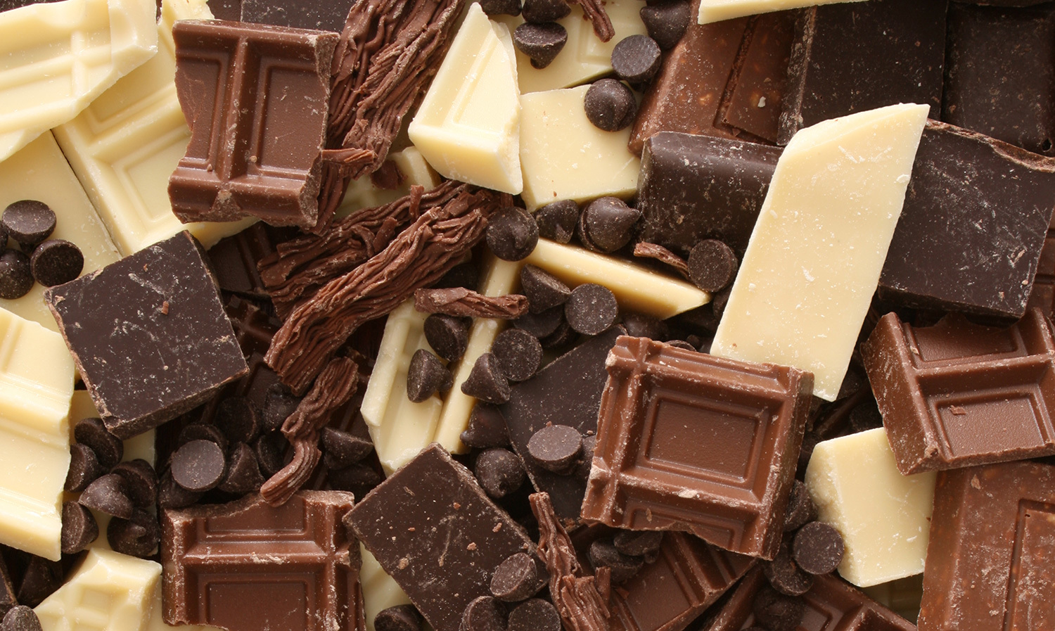 Assorted white, milk, and dark chocolate pieces with chocolate chips in a pile.