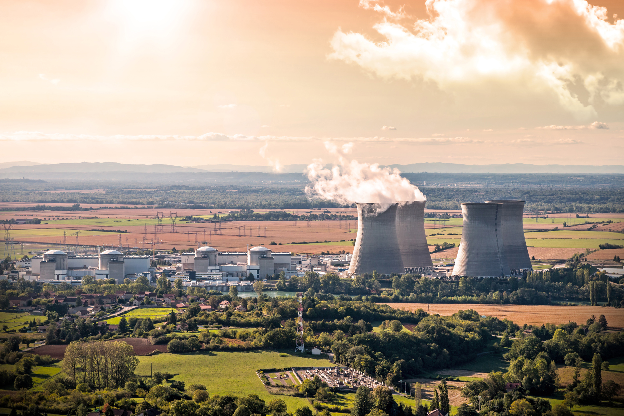 Nuclear power plant with cooling towers emitting steam in a rural landscape.