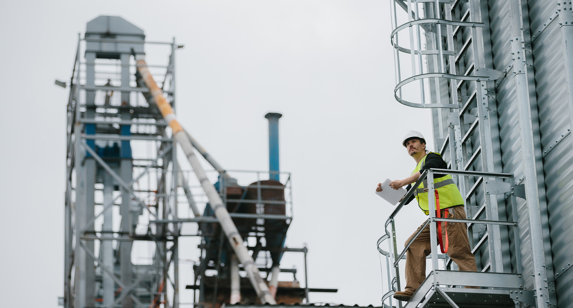 Construction worker in safety gear inspects industrial site from elevated platform.