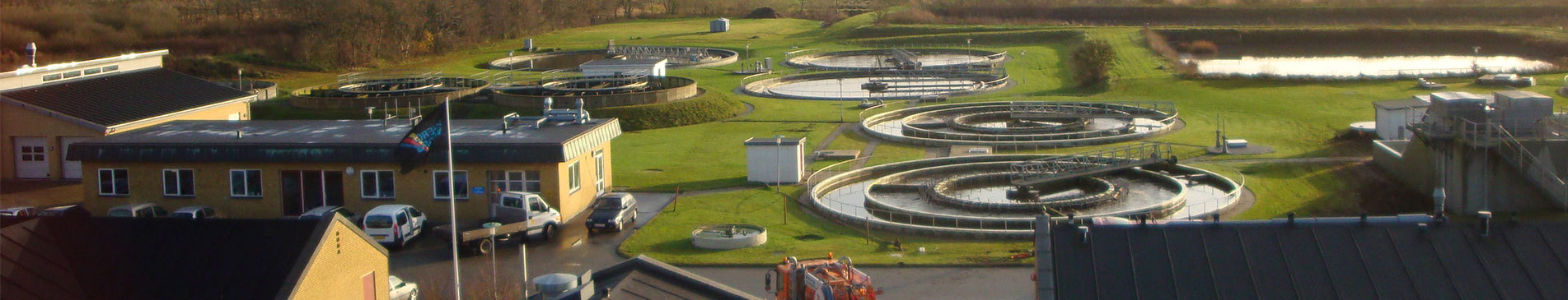 Aerial view of a water treatment facility with circular tanks and surrounding buildings.