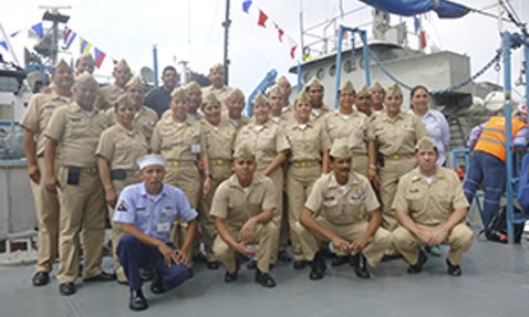 Group of uniformed personnel posing on a ship deck, with nautical flags above.