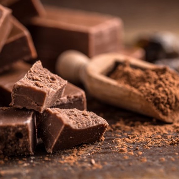 Chunks of chocolate and cocoa powder with a wooden scoop on a table.