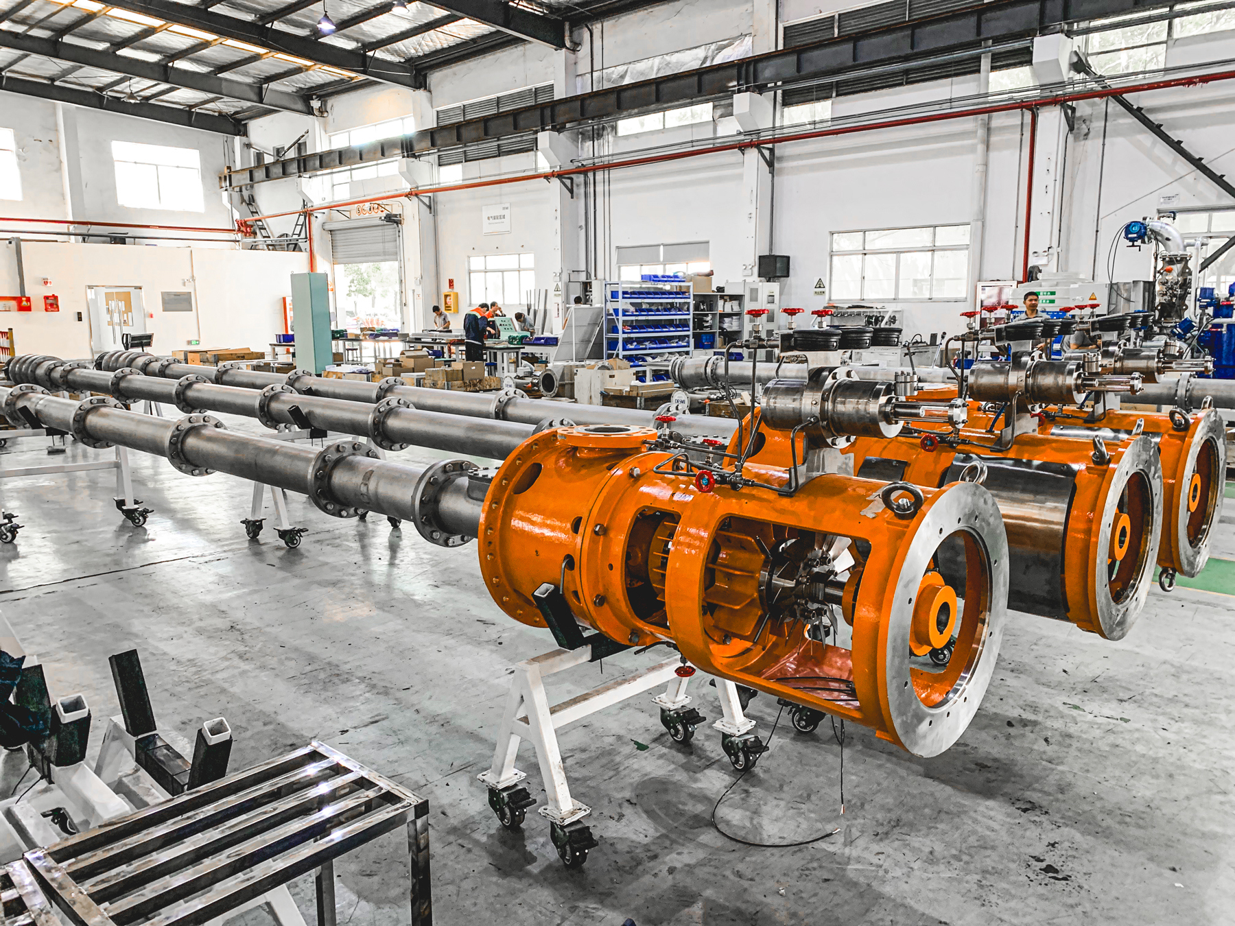 Industrial assembly line with large orange pumps, likely for fluid handling.
