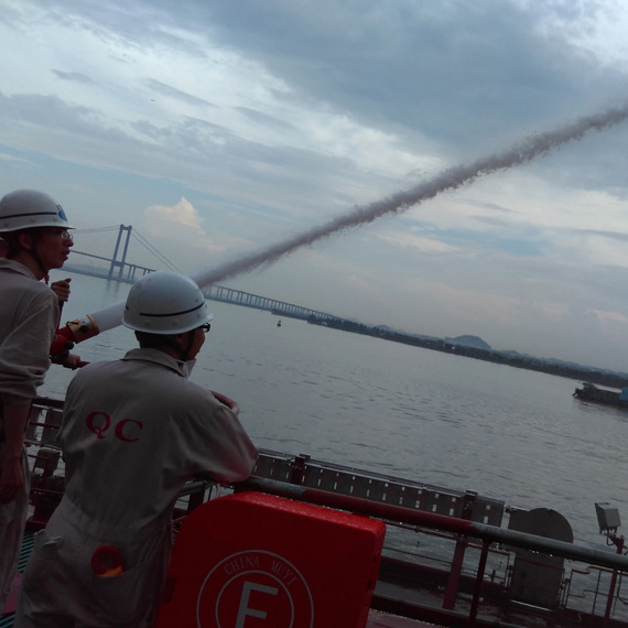 People using a fire hose on a boat, with a bridge in the background.