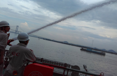 People using a fire hose on a boat, with a bridge in the background.