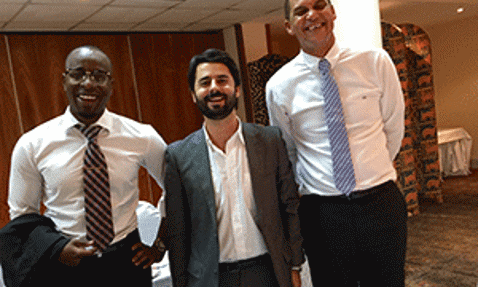 Three men in formal attire smiling in a conference room setting.