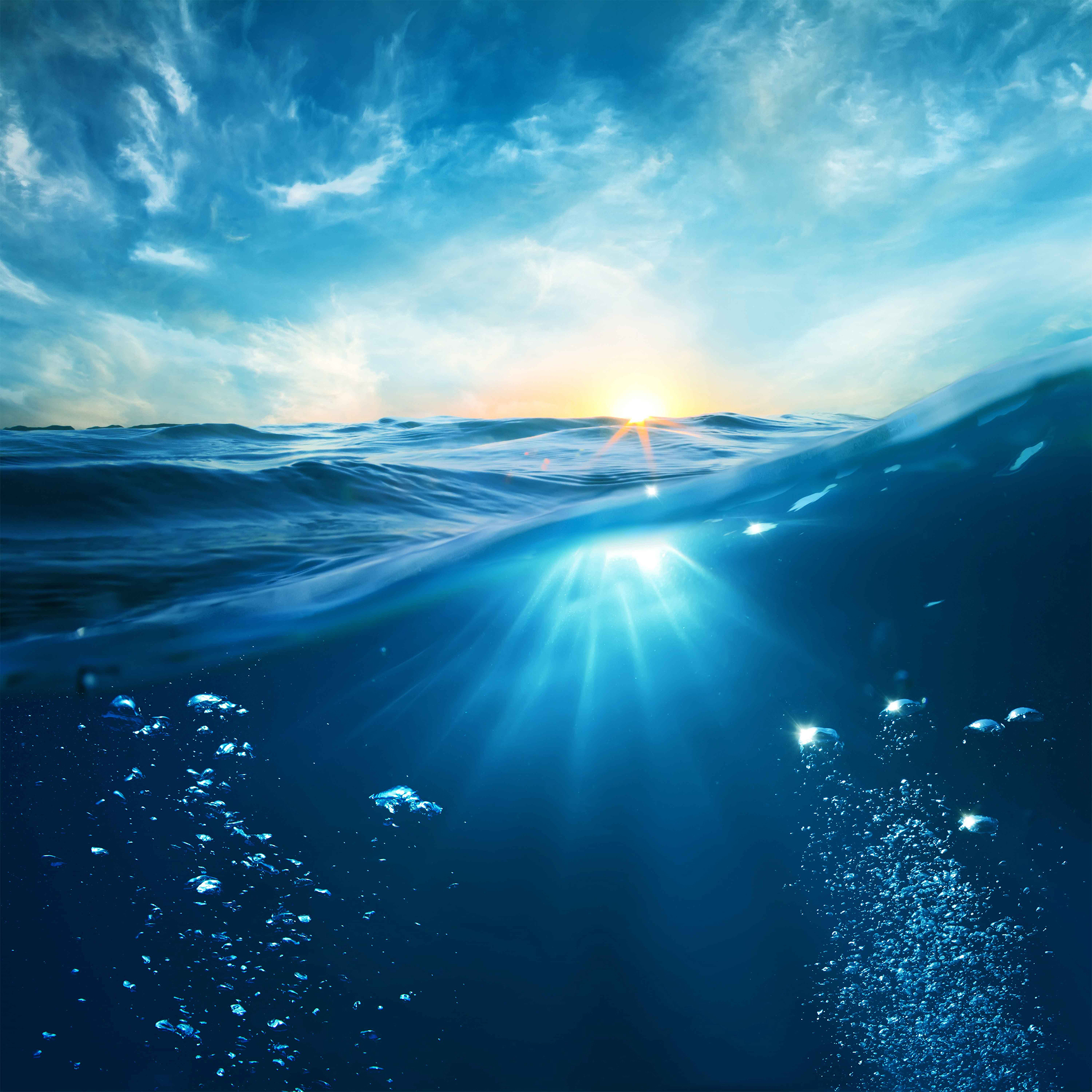 Sunset over ocean with underwater view and rising bubbles.