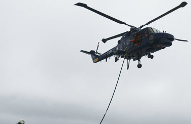 Helicopter refueling operation on a ship, two crew members handling hose.