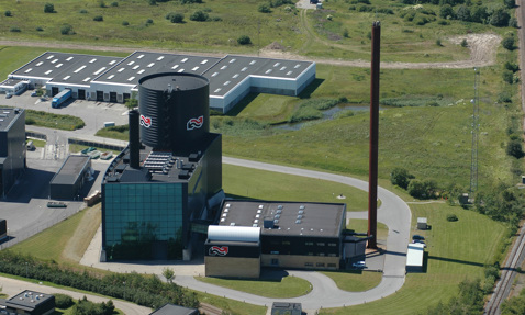 Aerial view of an industrial facility with large cylindrical structure and chimney.