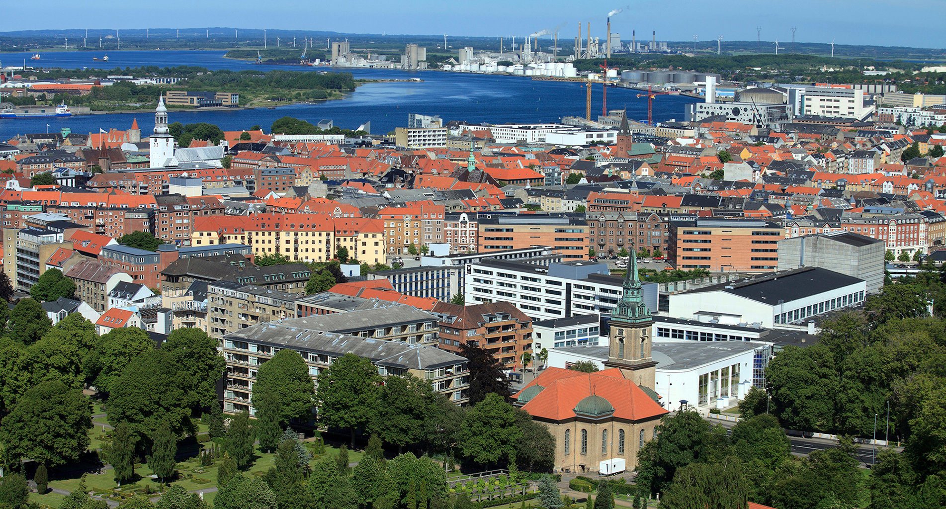 Aerial view of a coastal city with red-roofed buildings and industrial background.
