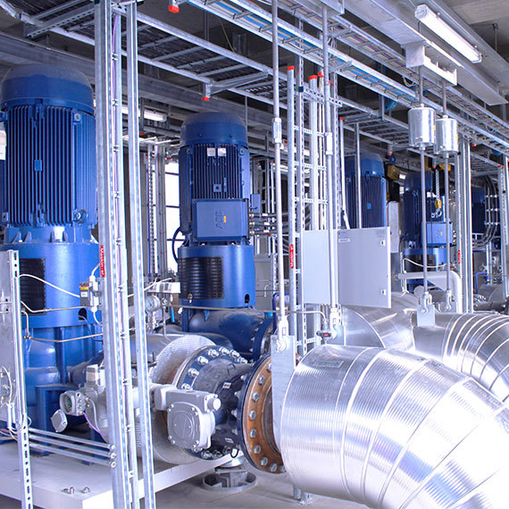 Industrial room with large blue DESMI pumps and metallic piping for fluid handling.