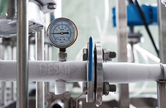 DESMI pressure gauge on frosted industrial pipe for fluid handling.