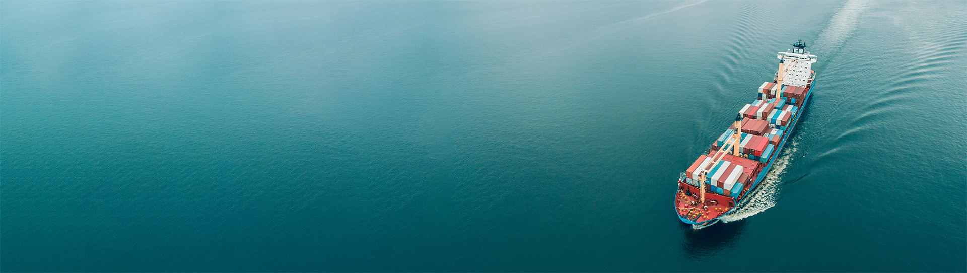 Cargo ship carrying containers sails through calm blue ocean waters.