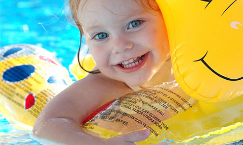 Smiling child with inflatable toy in a swimming pool.